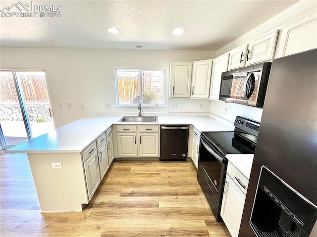 kitchen with light hardwood / wood-style floors, sink, kitchen peninsula, white cabinets, and appliances with stainless steel finishes