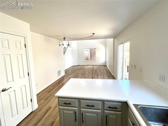 kitchen featuring an inviting chandelier, gray cabinets, kitchen peninsula, and hardwood / wood-style flooring