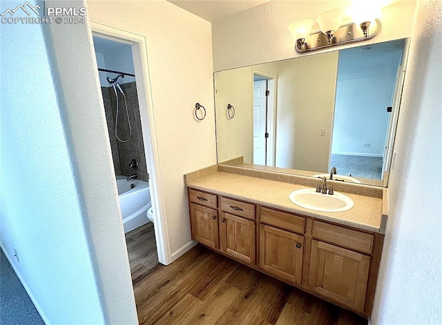 full bathroom featuring wood-type flooring, tiled shower / bath, vanity, and toilet