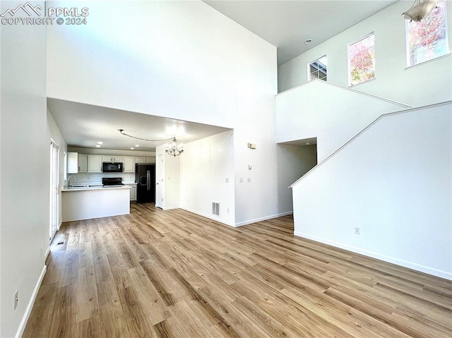 unfurnished living room with a towering ceiling, a chandelier, sink, and light wood-type flooring