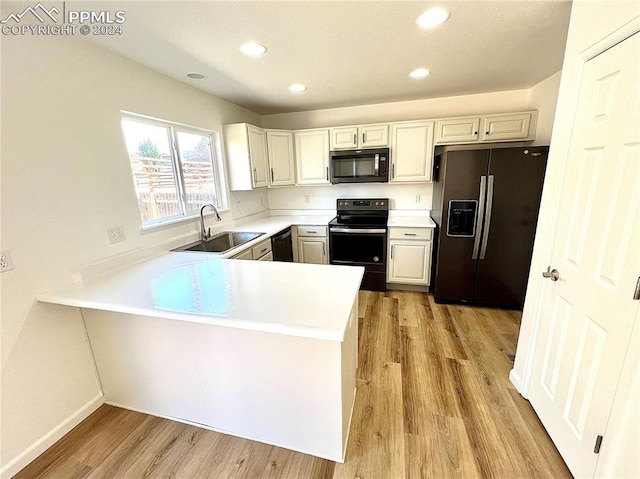 kitchen with light wood-type flooring, black appliances, sink, kitchen peninsula, and white cabinetry