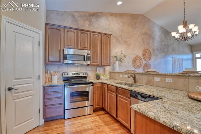 kitchen with appliances with stainless steel finishes, sink, light stone countertops, vaulted ceiling, and light hardwood / wood-style flooring