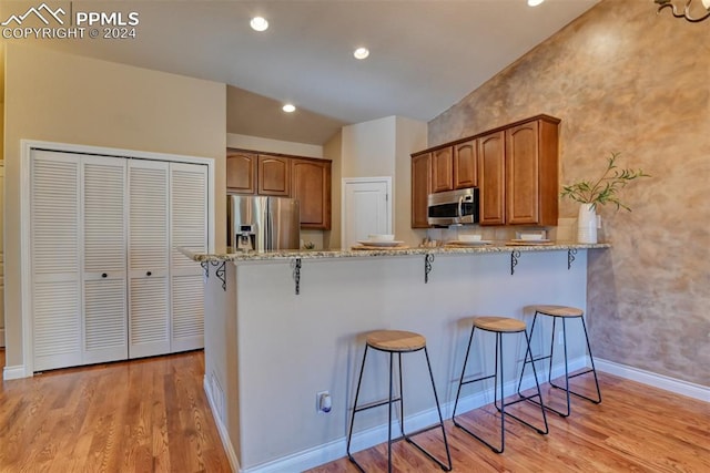 kitchen with light hardwood / wood-style floors, stainless steel appliances, lofted ceiling, light stone counters, and a breakfast bar area