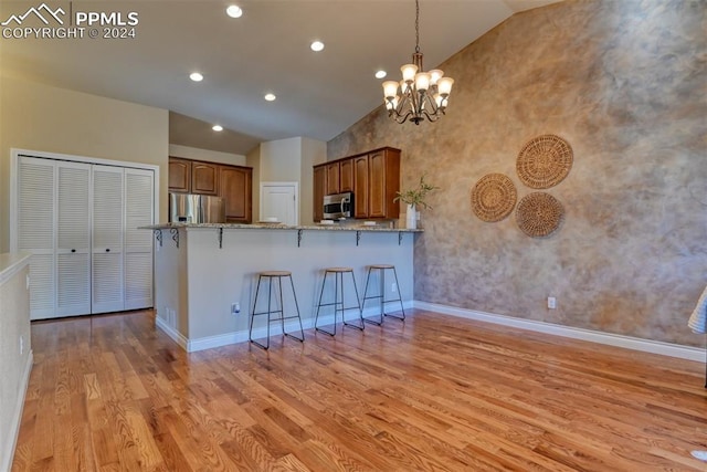 kitchen featuring kitchen peninsula, appliances with stainless steel finishes, a kitchen bar, light hardwood / wood-style flooring, and light stone counters