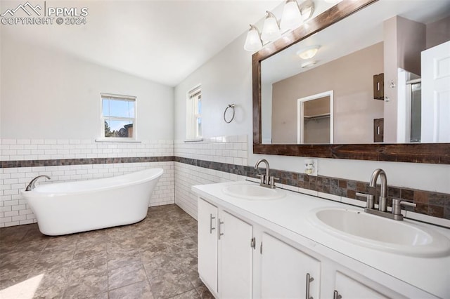 bathroom with a sink, a freestanding tub, vaulted ceiling, and tile walls