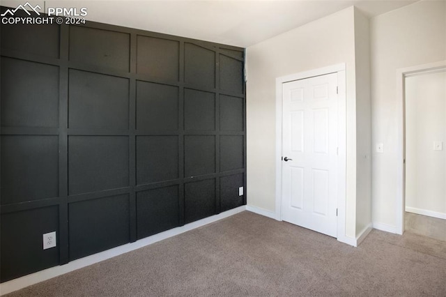 unfurnished bedroom with baseboards, carpet, and a decorative wall