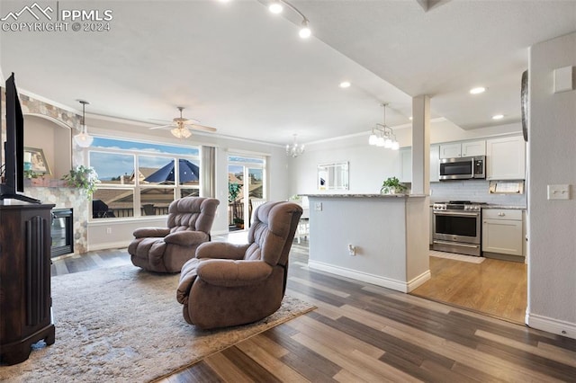 living room with wood-type flooring, ceiling fan with notable chandelier, and ornamental molding