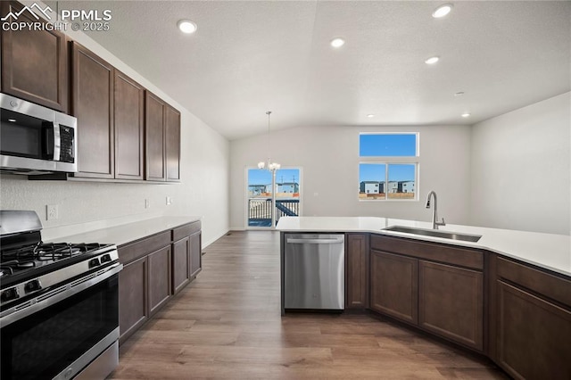 kitchen with light wood-style flooring, stainless steel appliances, a sink, hanging light fixtures, and light countertops