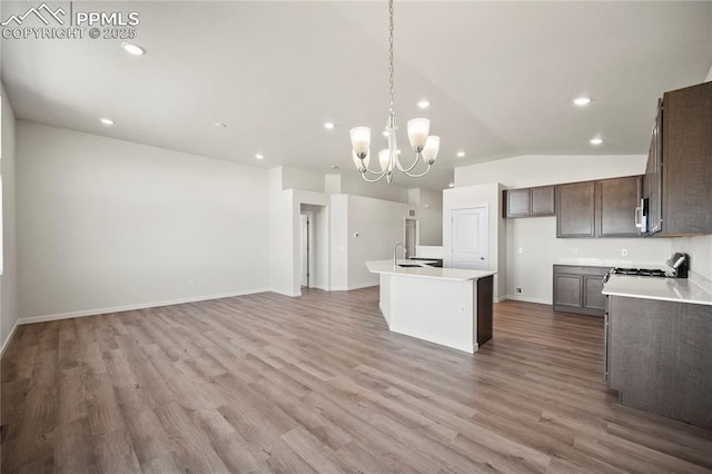 kitchen featuring a center island with sink, lofted ceiling, light countertops, hanging light fixtures, and wood finished floors