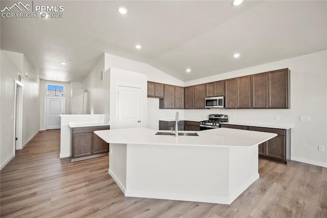 kitchen with stainless steel appliances, light countertops, a kitchen island with sink, a sink, and light wood-type flooring