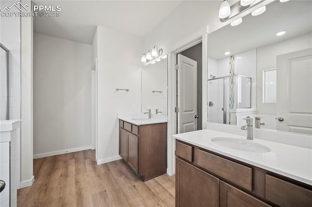 full bathroom featuring a stall shower, two vanities, a sink, and wood finished floors