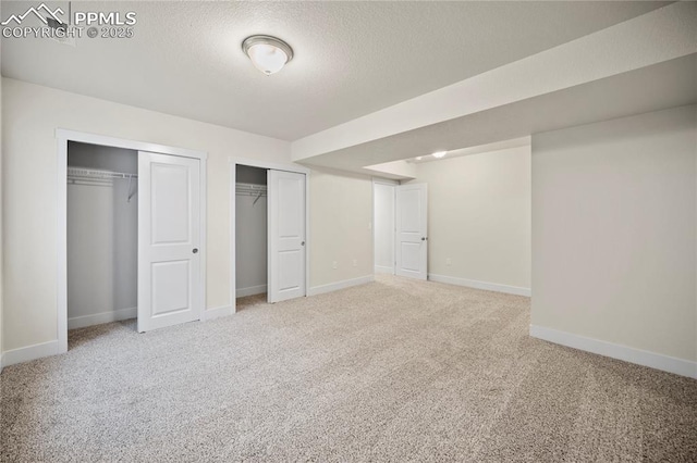 unfurnished bedroom with carpet flooring, a textured ceiling, baseboards, and two closets