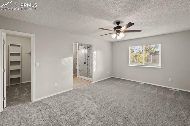 unfurnished bedroom featuring a closet, a walk in closet, a textured ceiling, carpet flooring, and ceiling fan