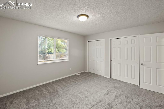 unfurnished bedroom with a textured ceiling, two closets, and carpet floors