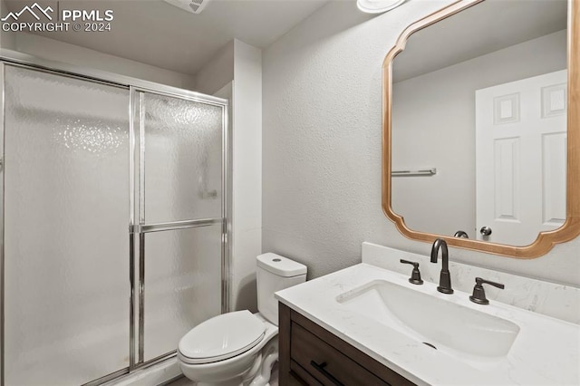 bathroom featuring a shower with door, vanity, and toilet