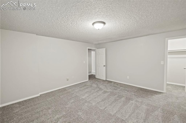 unfurnished bedroom featuring a closet, a textured ceiling, carpet floors, and a walk in closet