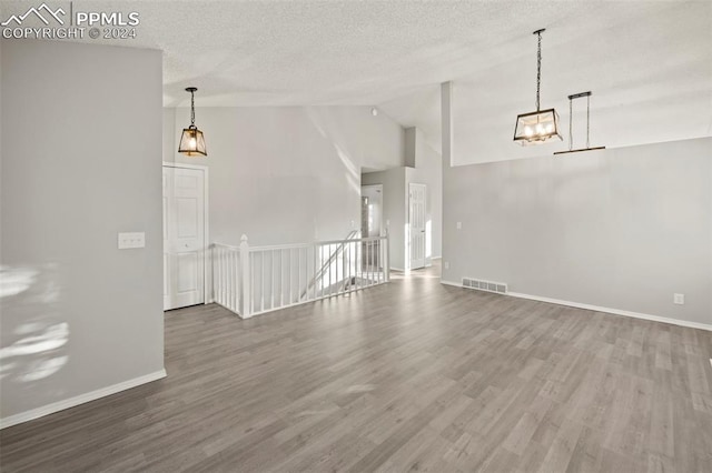 unfurnished living room with hardwood / wood-style flooring, a textured ceiling, and an inviting chandelier