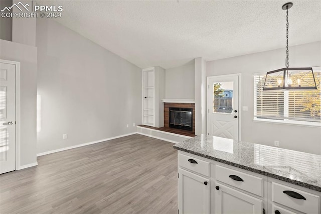 kitchen with a textured ceiling, wood-type flooring, decorative light fixtures, and white cabinets