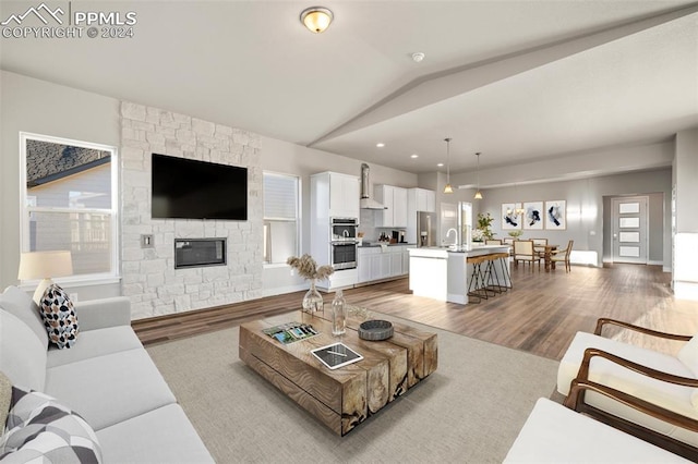 living room featuring a stone fireplace, a healthy amount of sunlight, vaulted ceiling, and light wood-type flooring