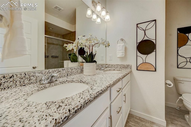 bathroom with toilet, hardwood / wood-style flooring, vanity, and a shower with door