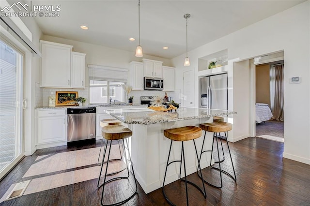 kitchen with appliances with stainless steel finishes, white cabinetry, dark hardwood / wood-style floors, pendant lighting, and a center island