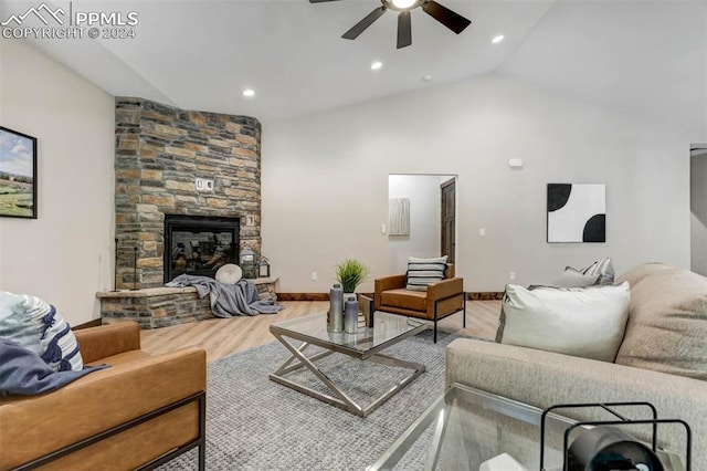 living room featuring wood-type flooring, ceiling fan, vaulted ceiling, and a stone fireplace