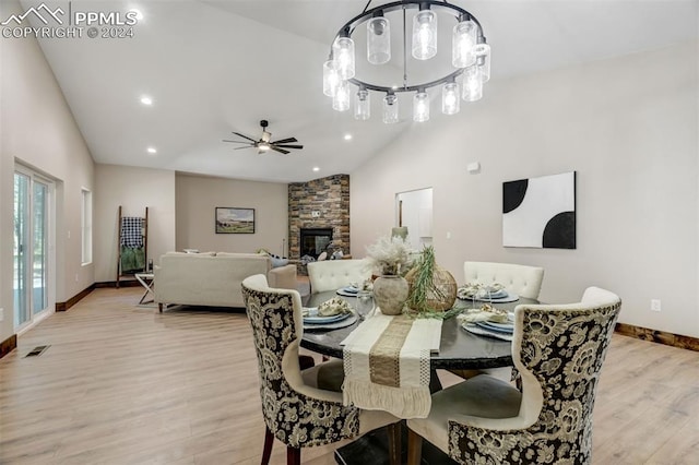 dining room with ceiling fan with notable chandelier, a fireplace, high vaulted ceiling, and light hardwood / wood-style flooring