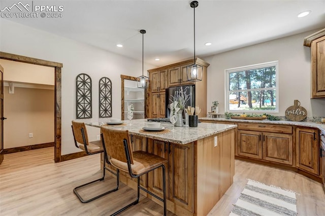 kitchen featuring stainless steel refrigerator, pendant lighting, a kitchen island, light hardwood / wood-style flooring, and light stone counters