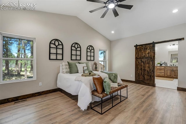 bedroom with light wood-type flooring, multiple windows, a barn door, and vaulted ceiling