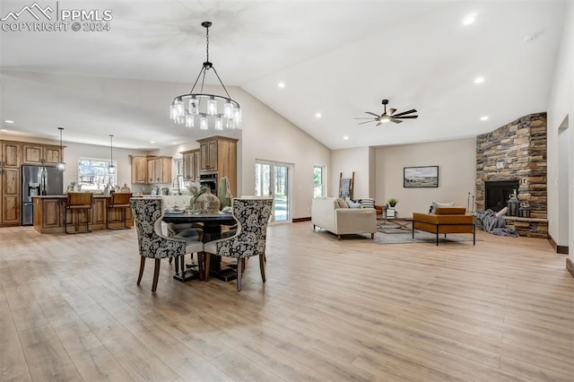 dining space with ceiling fan with notable chandelier, light wood-type flooring, a healthy amount of sunlight, and a fireplace