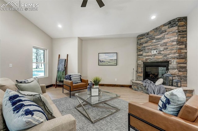 living room with lofted ceiling, ceiling fan, a stone fireplace, and light wood-type flooring