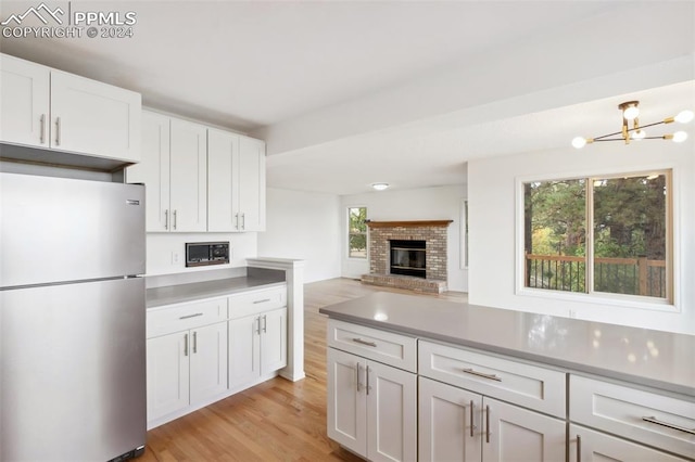 kitchen featuring stainless steel fridge, an inviting chandelier, light wood-type flooring, white cabinets, and a fireplace