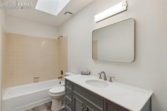 full bathroom featuring wood-type flooring, a skylight, toilet, tiled shower / bath, and vanity