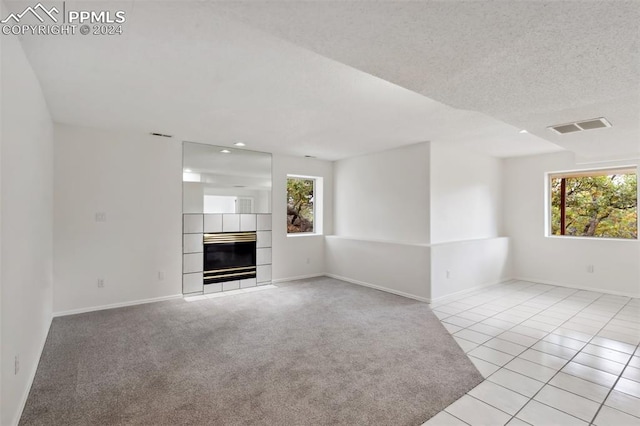 unfurnished living room with a textured ceiling, a tile fireplace, and light colored carpet