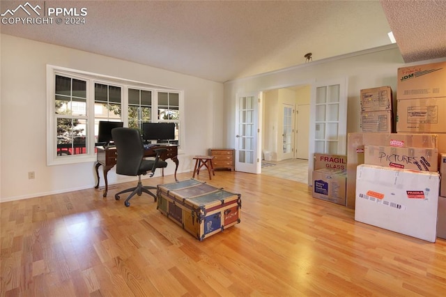 office space featuring lofted ceiling, french doors, a textured ceiling, and light hardwood / wood-style floors