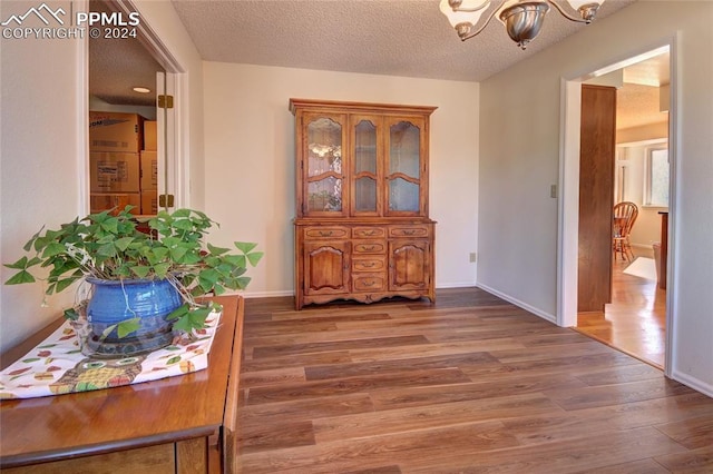 hall featuring a textured ceiling, an inviting chandelier, and dark hardwood / wood-style flooring