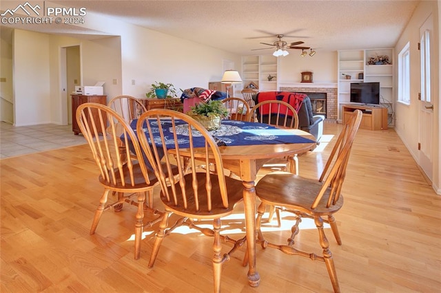 dining room with ceiling fan, a textured ceiling, light hardwood / wood-style flooring, and a brick fireplace