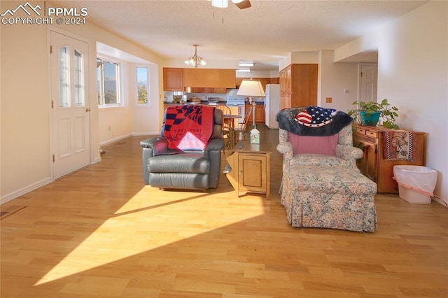 living area featuring light hardwood / wood-style floors, a textured ceiling, and ceiling fan with notable chandelier