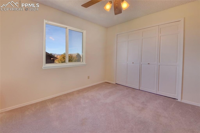 unfurnished bedroom with a textured ceiling, light colored carpet, a closet, and ceiling fan