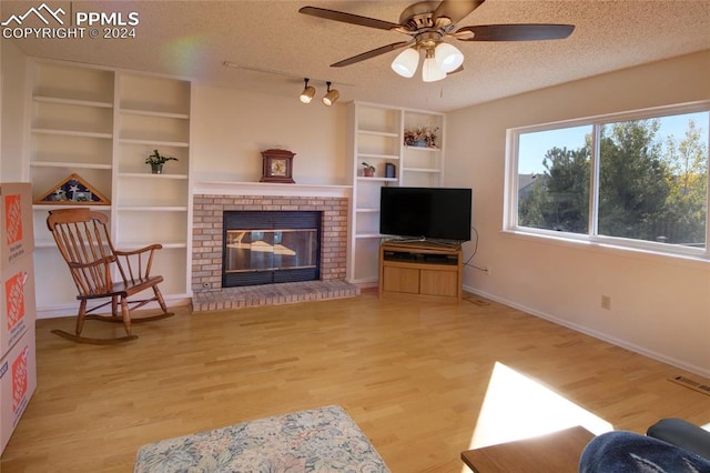 living room featuring ceiling fan, a textured ceiling, light hardwood / wood-style flooring, and a brick fireplace