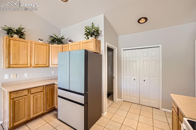 kitchen with light brown cabinets, light tile patterned floors, stainless steel fridge, vaulted ceiling, and range