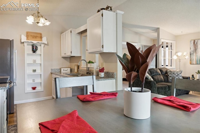 kitchen featuring white cabinets, vaulted ceiling, pendant lighting, a notable chandelier, and sink