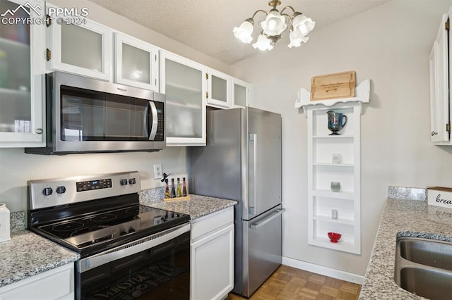 kitchen with white cabinets, an inviting chandelier, appliances with stainless steel finishes, light stone counters, and a textured ceiling