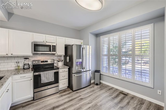 kitchen featuring stainless steel appliances, light stone countertops, light wood-type flooring, white cabinetry, and tasteful backsplash