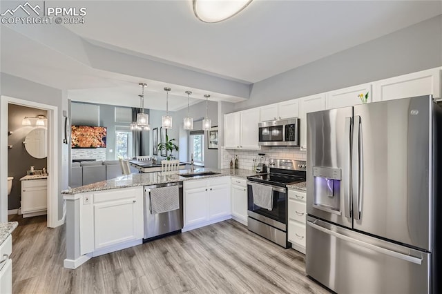 kitchen with appliances with stainless steel finishes, kitchen peninsula, white cabinetry, decorative light fixtures, and light hardwood / wood-style flooring