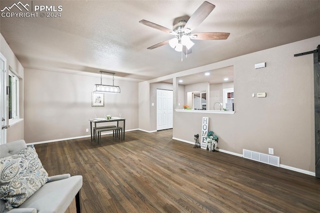 sitting room with a textured ceiling, a barn door, ceiling fan, and dark hardwood / wood-style flooring