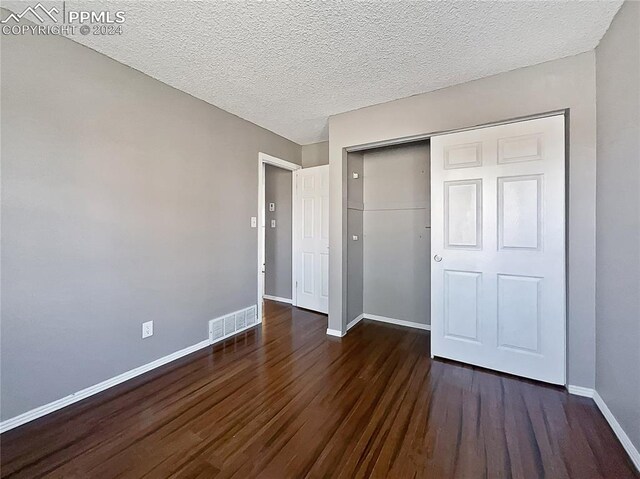 unfurnished bedroom with a closet, a textured ceiling, and dark hardwood / wood-style flooring