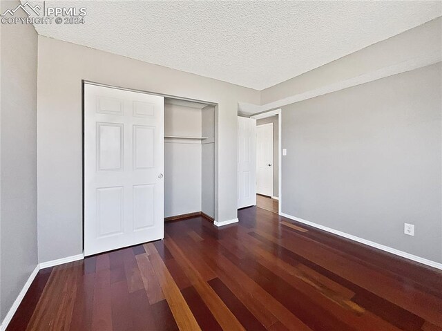 unfurnished bedroom with a textured ceiling, dark hardwood / wood-style floors, and a closet