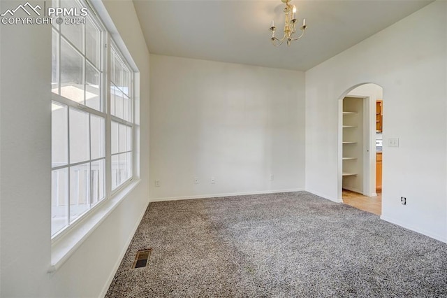 empty room with carpet, a healthy amount of sunlight, and an inviting chandelier