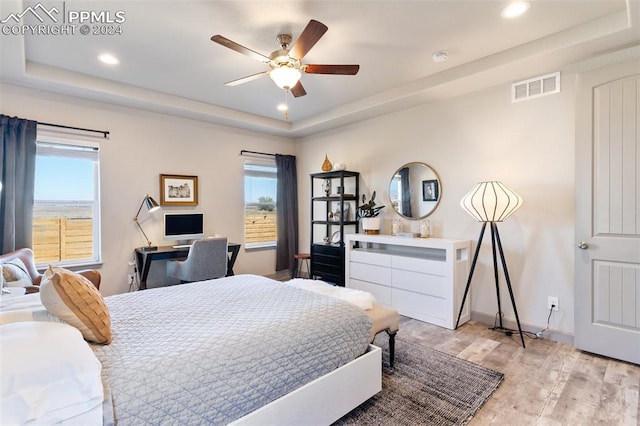 bedroom with a raised ceiling, light wood-type flooring, and ceiling fan